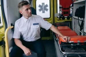 Paramedic seated inside an ambulance next to an empty gurney, completing documentation